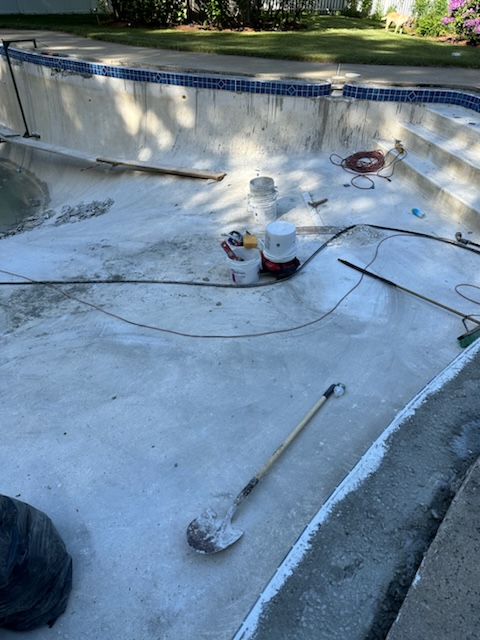 Empty swimming pool under maintenance with construction tools, buckets, and equipment scattered on the pool floor.