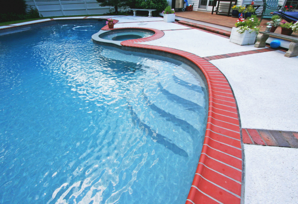 Curved swimming pool with built-in hot tub, red brick trim by expert pool coping installers in Pepperrell.
