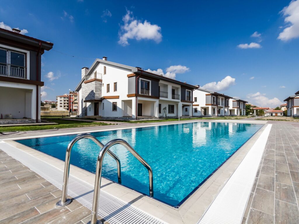 Outdoor swimming pool with metal ladder next to modern two-story white houses under a clear blue sky.