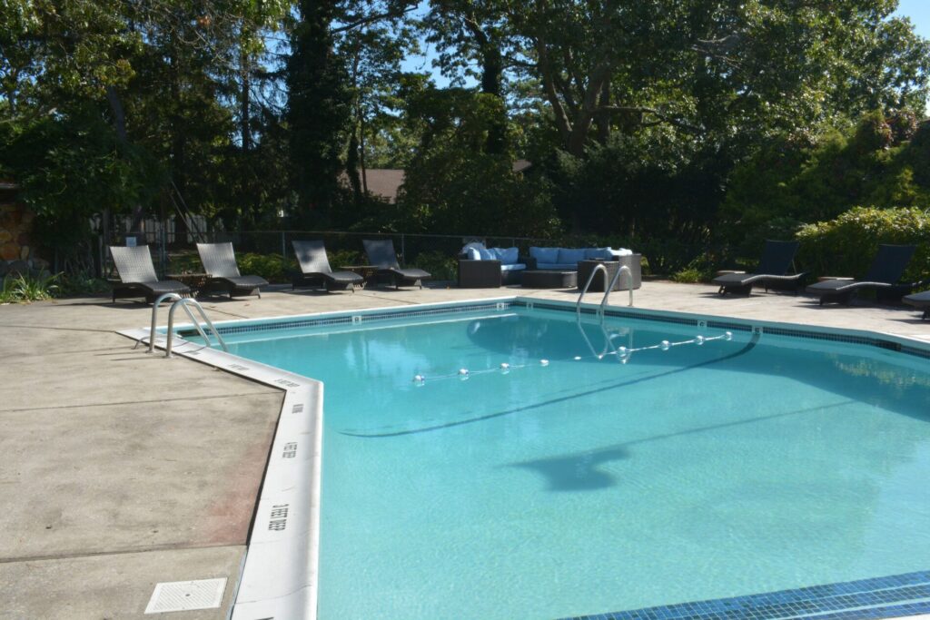 Outdoor swimming pool with clear water, surrounded by lounge chairs and greenery under bright sunlight.