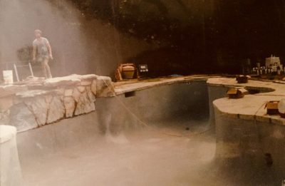 A person stands near the edge of an empty, unfinished swimming pool surrounded by construction materials.