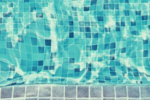 Close-up of a tiled swimming pool with clear blue water and sunlight creating reflections on the surface.